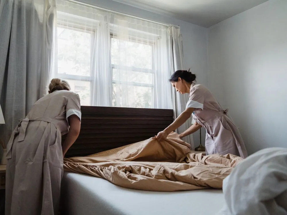 Deux gouvernantes refaisant un lit dans une chambre lumineuse